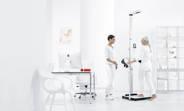 Ein Arzt und ein Patient stehen neben einem Bioimpedanzgerät für eine Messung der Körperzusammensetzung.
